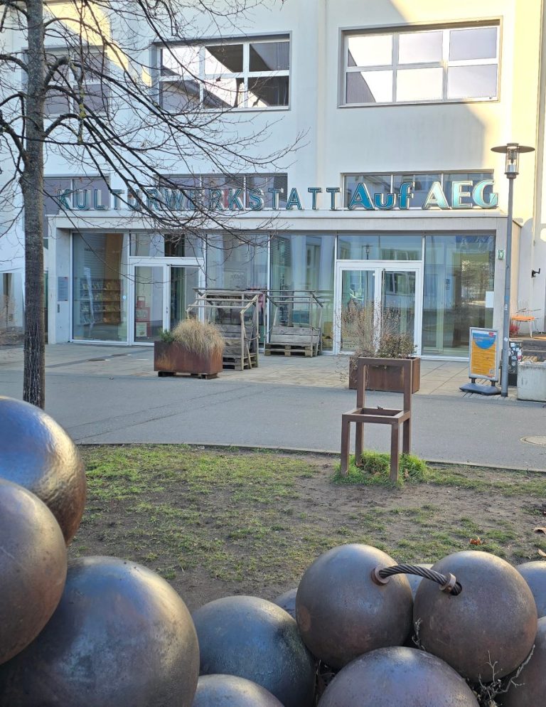Der Eingangsbereich der Kulturwerkstatt auf AEG. Im Vordergrund eine Skulptur aus Metallkugeln und ein Metallstuhl.
