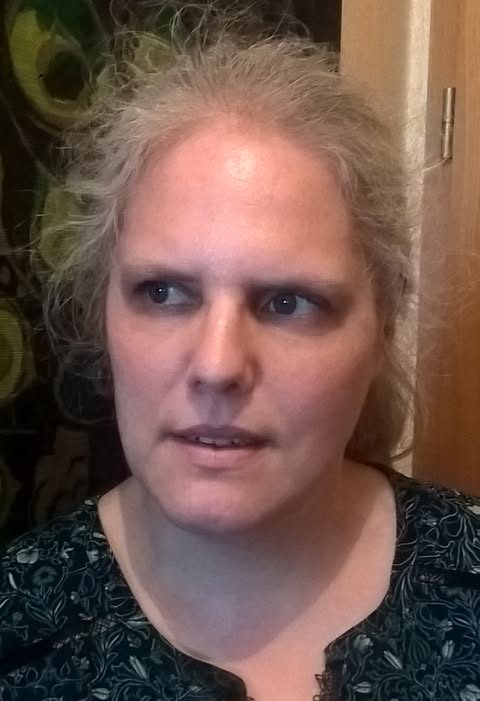 Eine blonde Frau, die ihre Haare im Pferdeschwanz trägt, schaut nachdenklich. Ihr Blick geht an der Kamera vorbei.