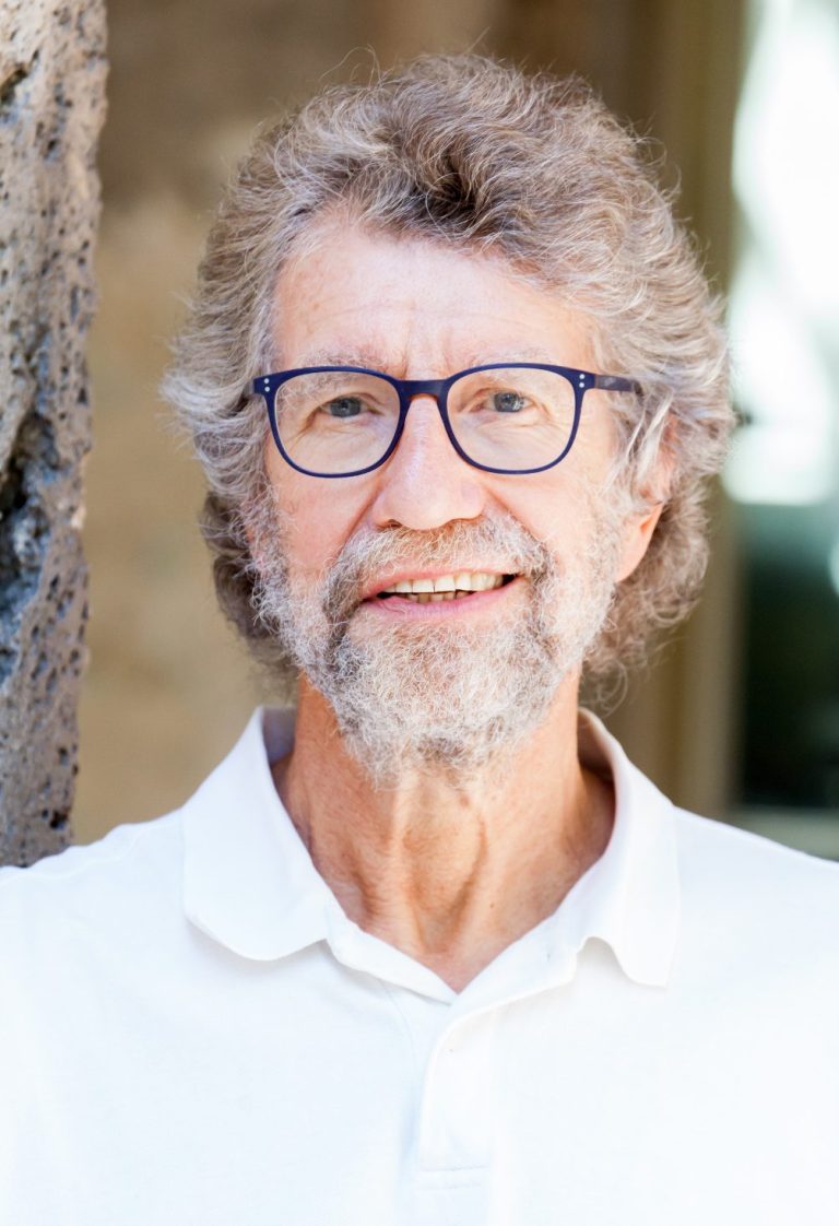 Ein Mann mit grauem Haar, Bart und Brille lächelt in die Kamera.