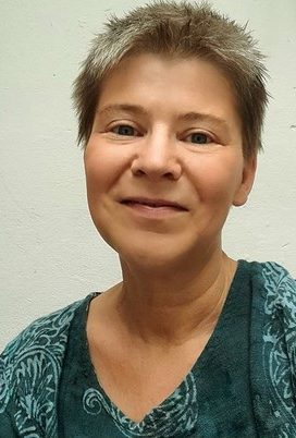 Eine Frau mit kurzen Haaren lächelt freundlich in die Kamera.